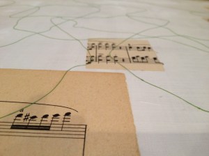 A detail showing squares of sheet music and string adhered to the surface of the plexiglass